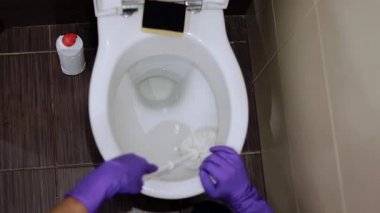 Bakış açısına göre, sarı eldivenli bir adam klozeti yıkıyor.