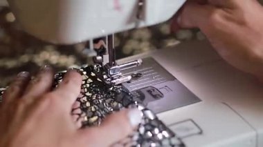 Dikiş makinesiyle maske takan bir kadın. Bu videoda, bir dikiş atölyesinde çalışma sürecine yakın çekim görüyoruz..