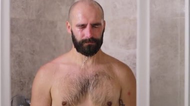 Depresyondaki adam duşta yıkanıyor, neşelenmeye çalışıyor. Banyoda sakallı yakışıklı adam suyun altında duş almaktan zevk alıyor. Sabah rutini.