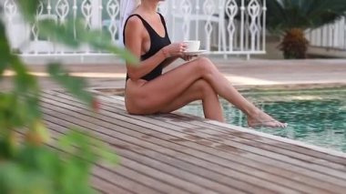 Zenginlik, güzellik ve rahatlama konsepti - Bornoz giyen, sabah kahvesini içen ve havuz ve villanın önünde sabahın tadını çıkaran zengin ve kendinden emin genç bir kızın portresi.