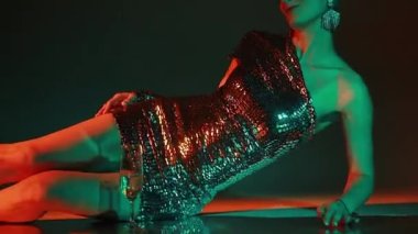 Güzel, ince, sarışın, parlak makyajlı, eski moda saç kesimli, gümüş renkli, parlak arka planda bir elbise giyen bir kız..