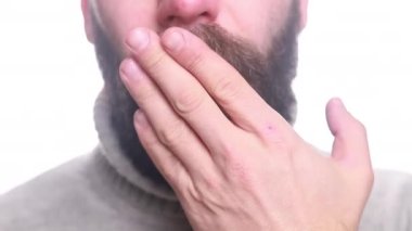 Genç yakışıklı beyaz adam burnunu kağıt peçeteye siliyor ve kendini çok kötü hissediyor. İnsan hasta, beyaz duvara karşı inliyor. Mevsimsel viral enfeksiyon.