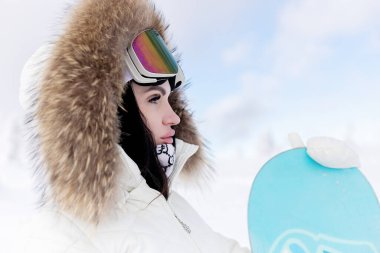 Kafasına Snowboard maskesi takmış güzel bir manken kadın portresi. Kar Maskeli Çekici Manken Sarışın Kar 'da oturuyor. Model, Snowboard ile kışın dinleniyor