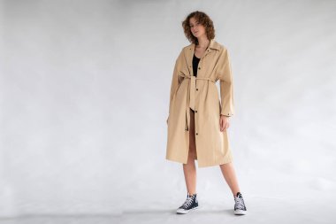 Gri arkaplanda Stüdyo 'da poz veren bej yağmurluklu güzel kız.