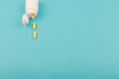 Sarı haplar ve plastik beyaz şişe. Metin için kopyalama alanı olan mavi arkaplan. Sağlıklı ve ilaç. Acı yönetimi. Gençlik kavramında uyuşturucu kullanımı