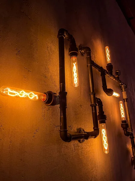 Retro lamp in steam punk style on the concrete wall indoors with light bulbs and pipes. Steampunk architectural style design element of interior. Grain effect, depth of field