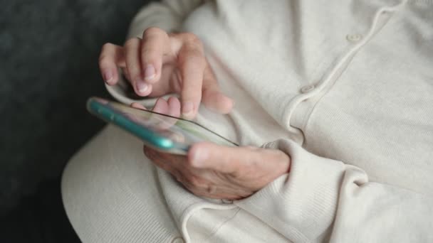 在亲戚朋友们赠送的现代品牌手机上 穿着柔软羊毛衫双手皱皱的老年妇女躺在滑行的页面上 — 图库视频影像