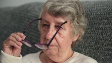 Yaşlı kadın görmek için gözlük takıyor kanepeye oturuyor.