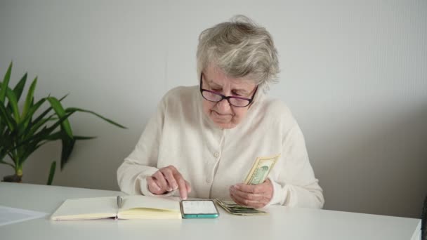 Mujer de pelo gris cuenta dinero distribuyendo pensión en la mesa — Vídeos de Stock
