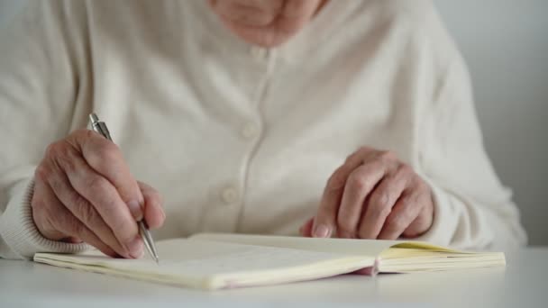 Vieille femme écrit des notes avec la main tremblante enlève des lunettes — Video