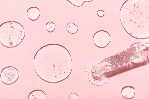 Yaşlanma önleyici emülsiyon damlaları ve açık pembe yüzeye yakın üst görüş için cam pipet ucu. Cilt bakımı ve dermatolojik prosedürler