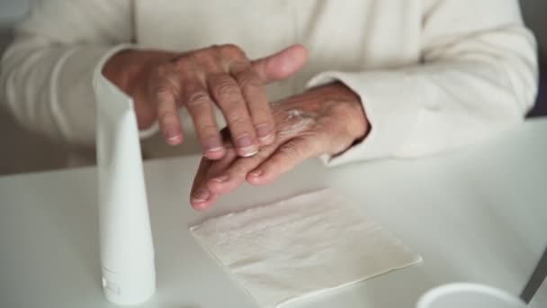 Staruszka z zmarszczkami kładzie krem nawilżający na dłonie — Wideo stockowe