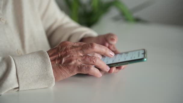 Staruszka z pomarszczonymi rękami ogląda media społecznościowe przez telefon — Wideo stockowe
