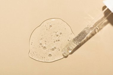 Bej yüzeyinde cam pipeti olan temiz bir serum döküldü.