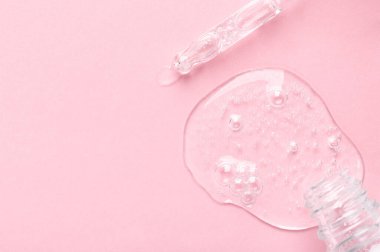 Açık pembe üzerinde berrak jöle olan küçük şişe ve cam pipet.