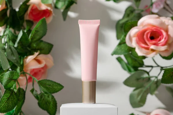 Kleine buis van natuurlijke huidverzorgingsproduct op podium en rozen Stockfoto