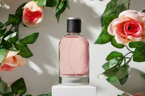 Frasco de vidrio de perfume de mujer en el podio en marco de rosas — Foto de Stock