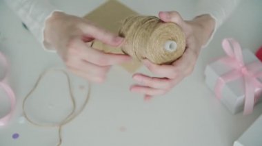 Beyaz ince gömlekli kadın tasarımcı bobbin açıyor ve karton kutu dekorasyonu için ince kabloyu keserken makas kullanıyor.
