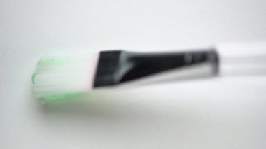 Beyaz zemin üzerinde küçük fırça ile yeşil temizleyici jel uygulamak aşırı yakın görüş. Refah için lüks kozmetik ürünü