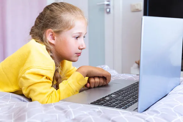 Una adolescente mirando la pantalla de su portátil mientras está acostada en la cama. — Foto de Stock