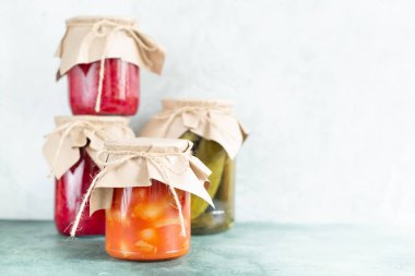 Açık yeşil arka planda cam kavanozlarda saklanmış sebzeler..