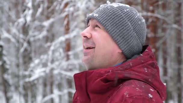 겨울 공원에 떨어지는 눈을 올려다보고 있는 미소짓고 있는 젊은 청년의 모습 — 비디오