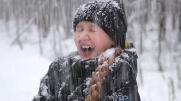 Sneeuw valt op het gezicht van een lachend tienermeisje in winterkleding, in een park. — Stockvideo