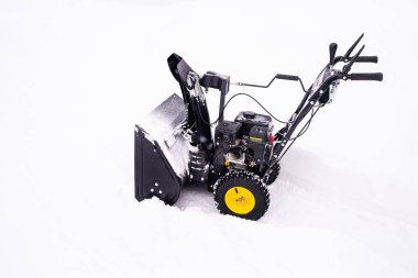 Black mini snowplow with yellow wheel on background of white snow.