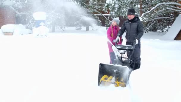 El hombre y su hija en nevadas en el patio quitan la nieve con el quitanieves juntos. — Vídeo de stock