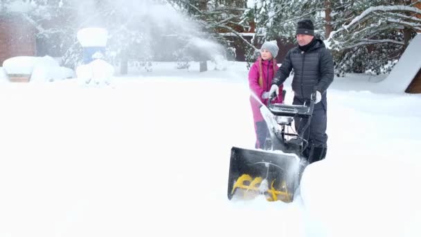 Man and his daughter in snowfall in yard remove snow with snowplow together. — Stockvideo