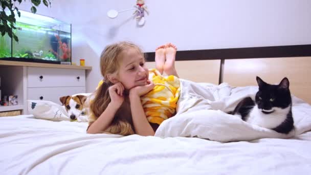 Menina 10-11 anos deitada na cama com animais de estimação, gato e cachorro, sorrindo, assistindo TV. — Vídeo de Stock