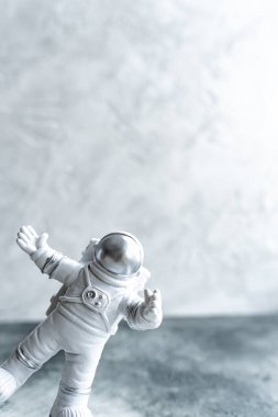 Uzay kıyafetli minyatür astronot elini gri arka planda sallıyor.