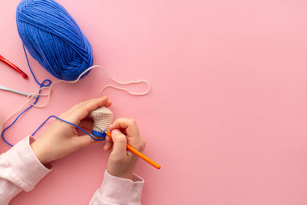 Childrens hands in the process of crocheting toys from blue and beige yarn.
