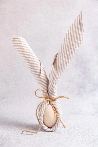 Ovo embrulhado em guardanapo de linho em forma de coelho da Páscoa com orelhas no fundo claro. — Fotografia de Stock