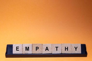 EMPATHY. Word written on square wooden tiles with an orange background. Horizontal photography.
