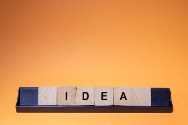 IDEA. Word written on square wooden tiles with an orange background. Horizontal photography.