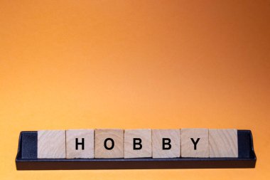 HOBBY. Word written on square wooden tiles with an orange background. Horizontal photography.
