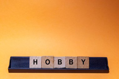 HOBBY. Word written on square wooden tiles with an orange background. Horizontal photography.