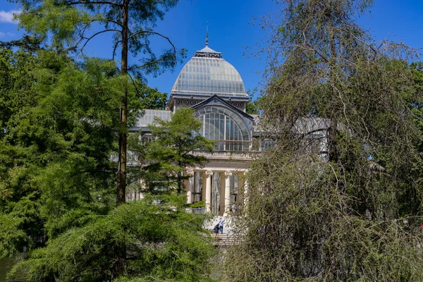 クリスタルパレス マドリードのレティーロ公園に位置する建物で 晴れた日には木々や緑の植生に囲まれたガラス窓と空のいくつかの雲 スペイン ヨーロッパだ — ストック写真