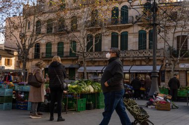 Llucmajor, İspanya; Ocak 07 2022: Majorcan kasabasındaki haftalık sokak pazarı. Coronavirus 'un Omicron versiyonunun kısıtlamalarından dolayı maskeli tedarikçiler ve müşteriler. Yeni normal