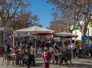 Llucmajor, İspanya; Ocak 07 2022: Güneşli bir sabah sabahı, Majorcan 'ın Llucmajor kasabasının meydanında maske takan müşterilerle dolu bir kafeteryanın terası