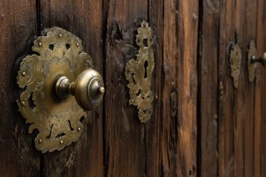 Close-up of an antique golden door handle made of metal, on a rustic wooden door