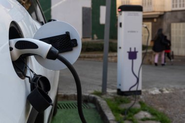 Caddeye park edilmiş beyaz elektrikli bir arabayı şarj eden bir şarj aletinin yakın çekimi. Yenilenebilir enerji görüntüsü