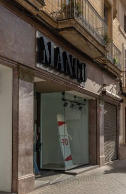 Manacor, İspanya; 20 Ocak 2022: Çok uluslu giyim ve aksesuar şirketi Mango 'nun cephesi, maske takan insanlarla güneşli bir sabah. Yeni normal