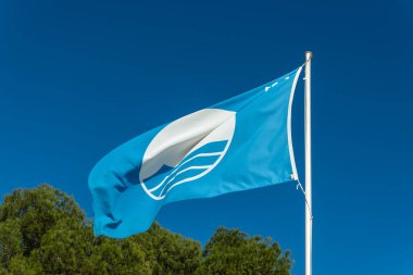 Blue flag of a beach on the island of Mallorca on a sunny day. Sign of good beach quality clipart