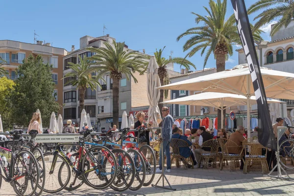 Felanitx, İspanya; 24 Nisan 2022: İspanya 'nın Felanitx kentinde güneşli bir pazar sabahı müşterilerle birlikte bir kafeteryanın terası. Bisikletçi mola veriyor.
