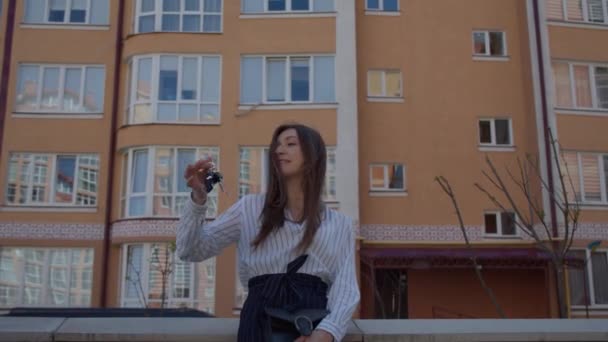 En ung kvinne viser nøkkelen til leiligheten sin foran huset.. – stockvideo
