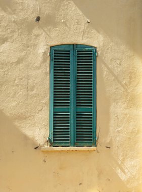 Old wooden window shutters closed against yellow wall.
