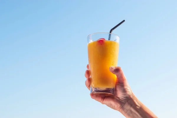 Woman\'s hand raising glass with refreshing orange cocktail in the air.