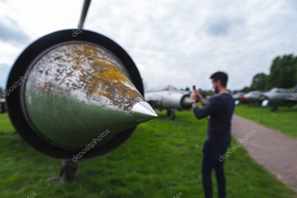 Pointy nose of a soviet fighter jet airplane, a man standing in the background taking a picture of the exhibits. Concept of aviation museums and tourists walking around